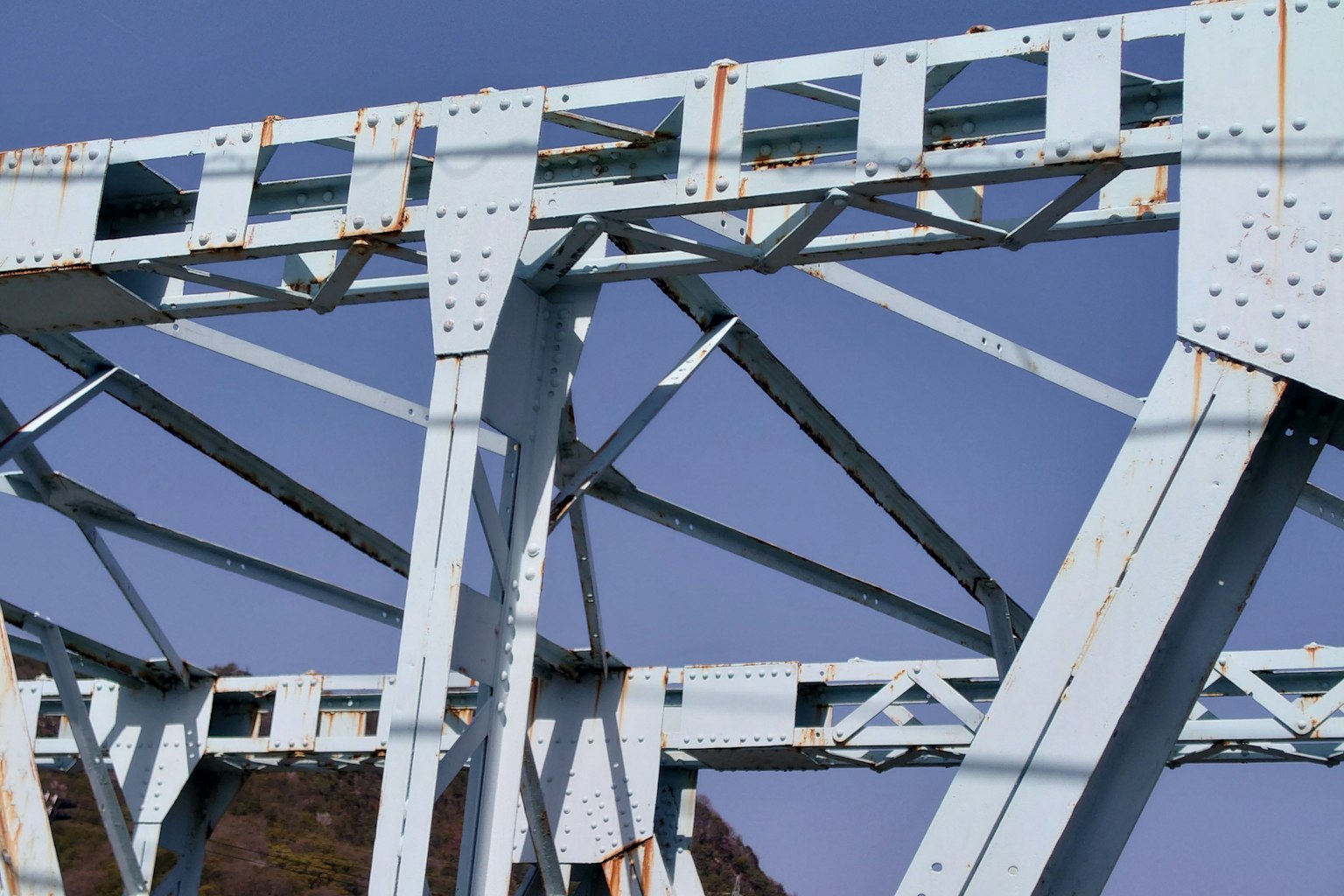 Structural details of a blue metal bridge against a clear sky