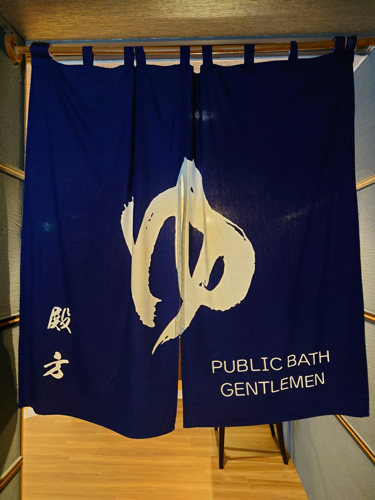 Noren biru dengan kanji '湯' dan teks 'PUBLIC BATH GENTLEMEN'