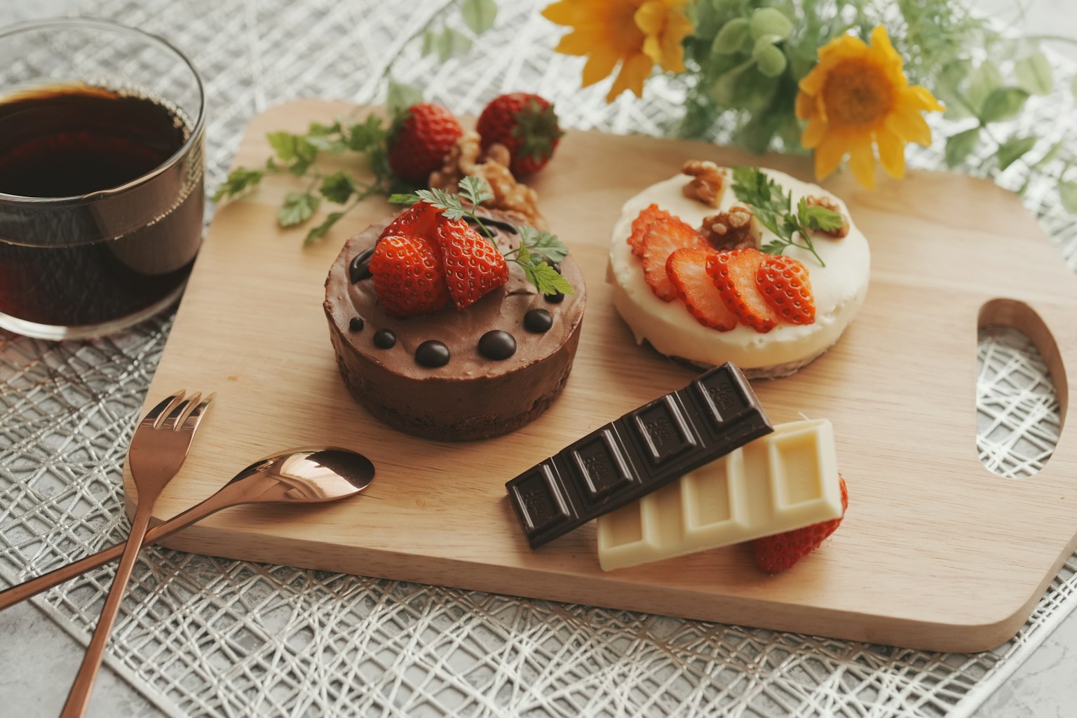 Una bandeja de madera con pastel de chocolate y tarta de frutas junto a una taza de café y girasoles