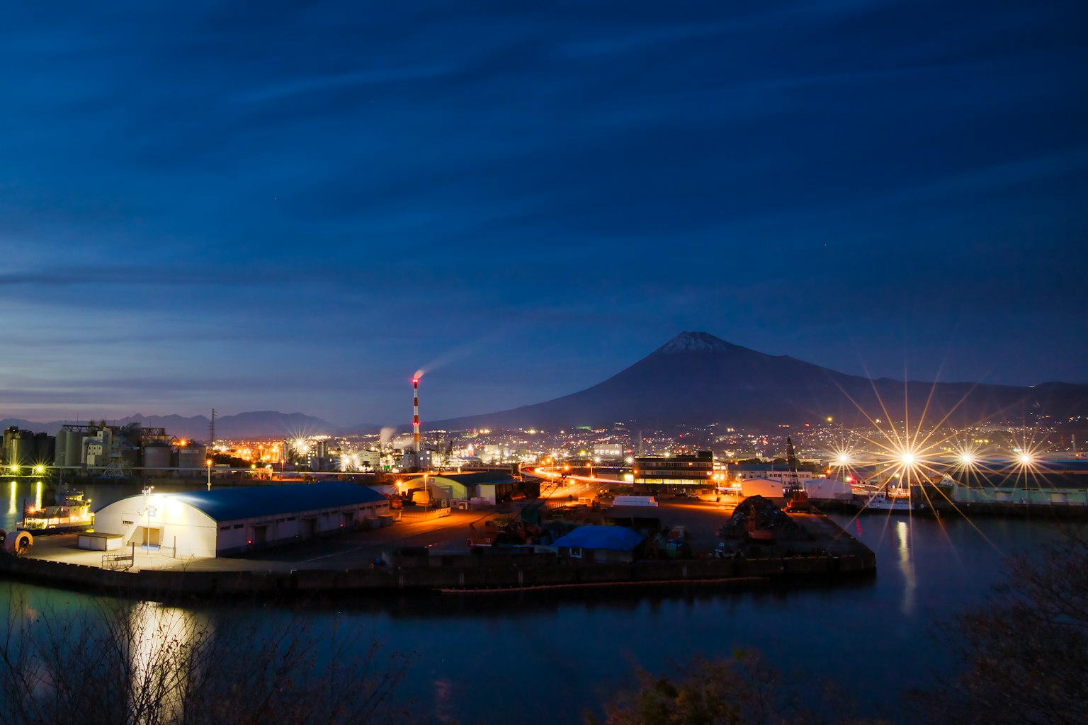 Night view of a harbor with a mountain factory lights and calm water surface