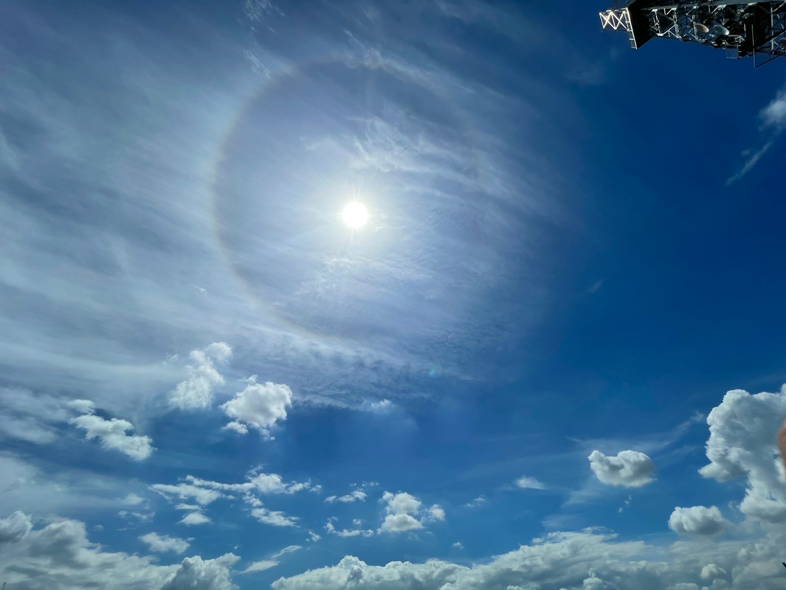 Sonne umgeben von einem kreisförmigen Halo in einem blauen Himmel mit dünnen Wolken