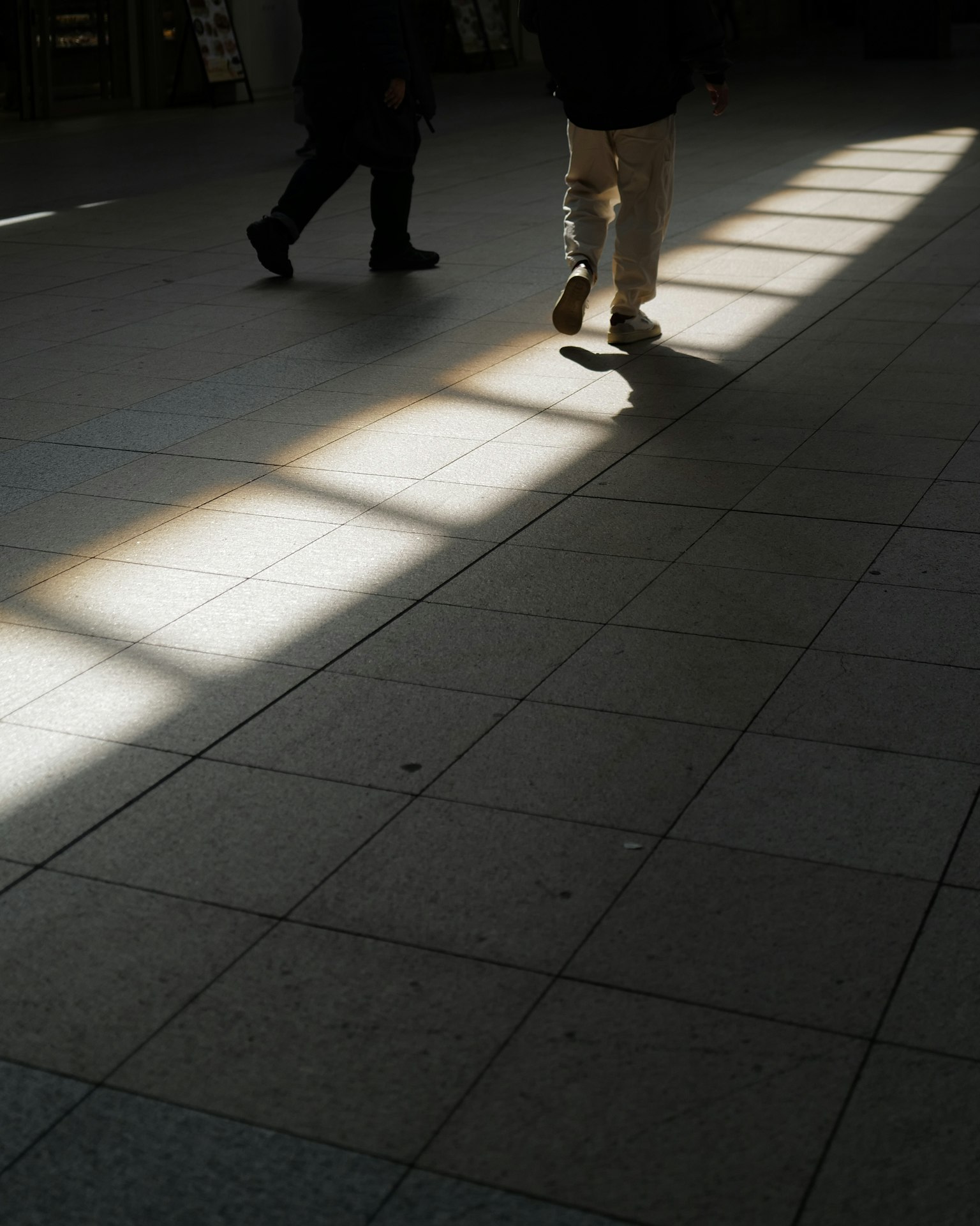 Silhouette di persone che camminano su un pavimento piastrellato con luce brillante che proietta ombre