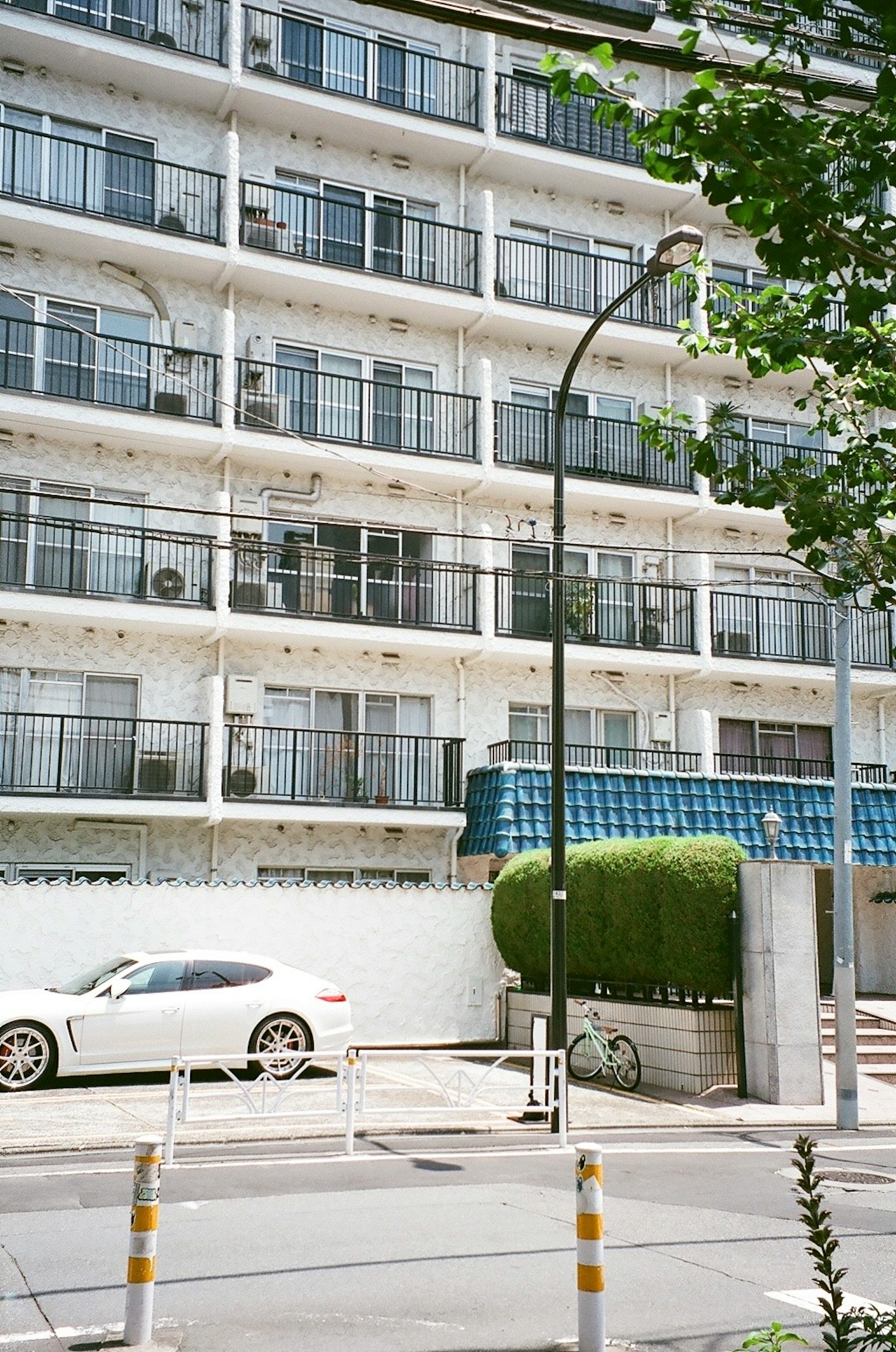 Exterior of an apartment building with a white car and green shrubbery