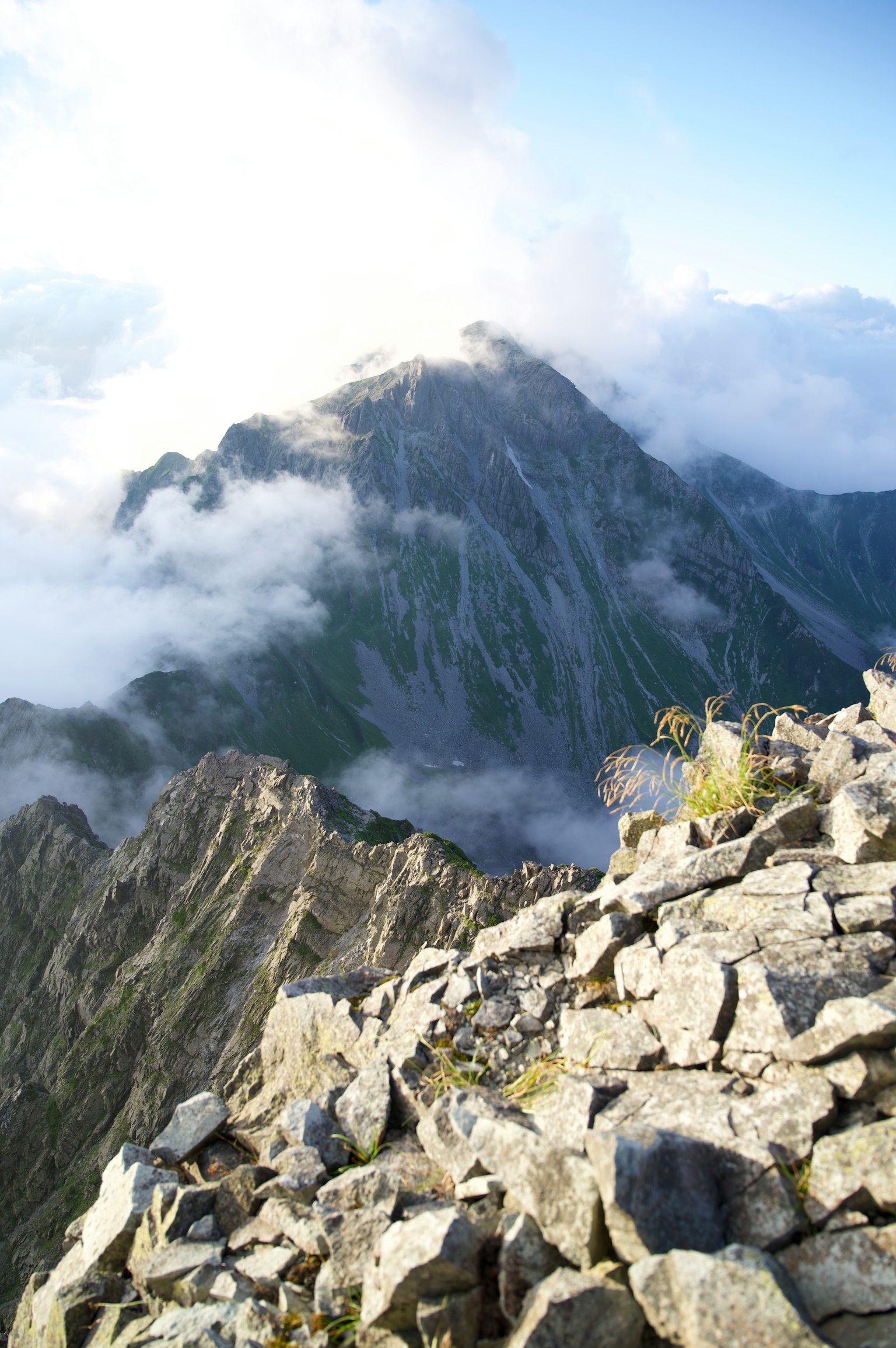 Aussicht vom Gipfel des Berges mit steinigem Gelände und von Wolken bedeckten Gipfeln