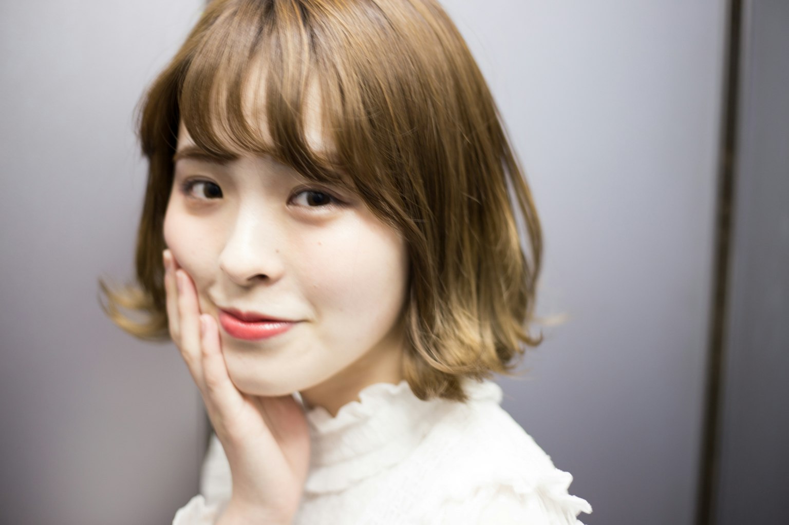 Une femme avec des cheveux clairs souriant en touchant son visage