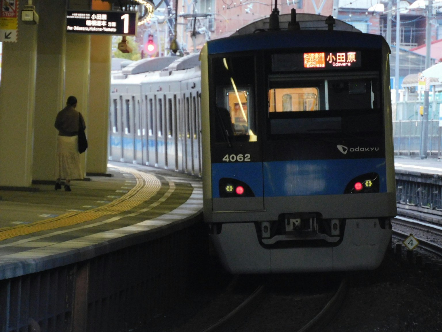 Tren azul llegando a una estación con un pasajero en el andén