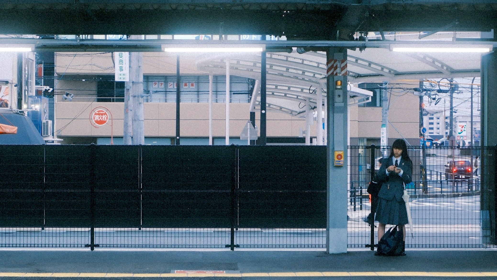 駅のホームで荷物を持つ人と高架の線路