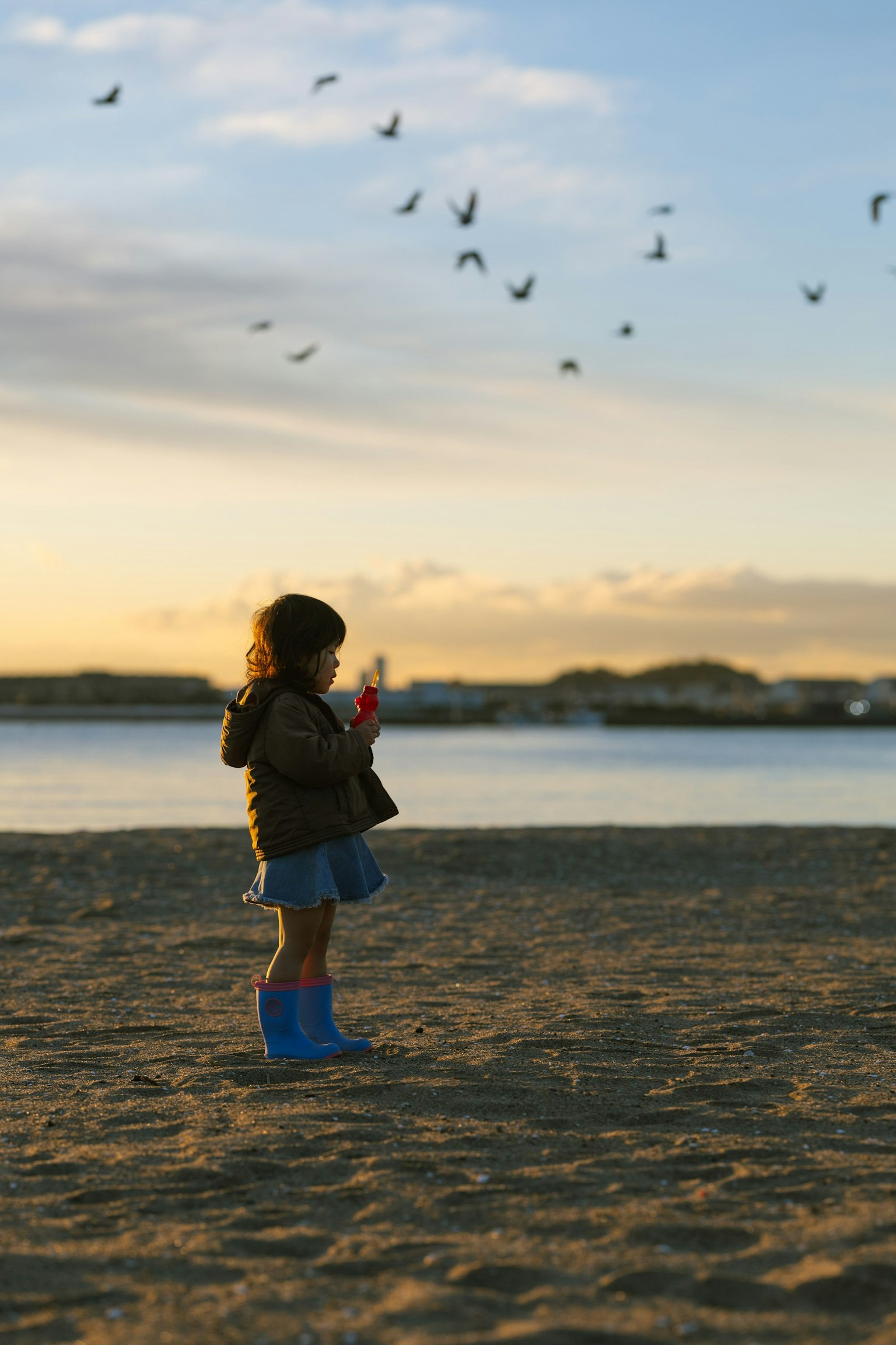 Anak berdiri di pantai melihat ke langit saat matahari terbenam