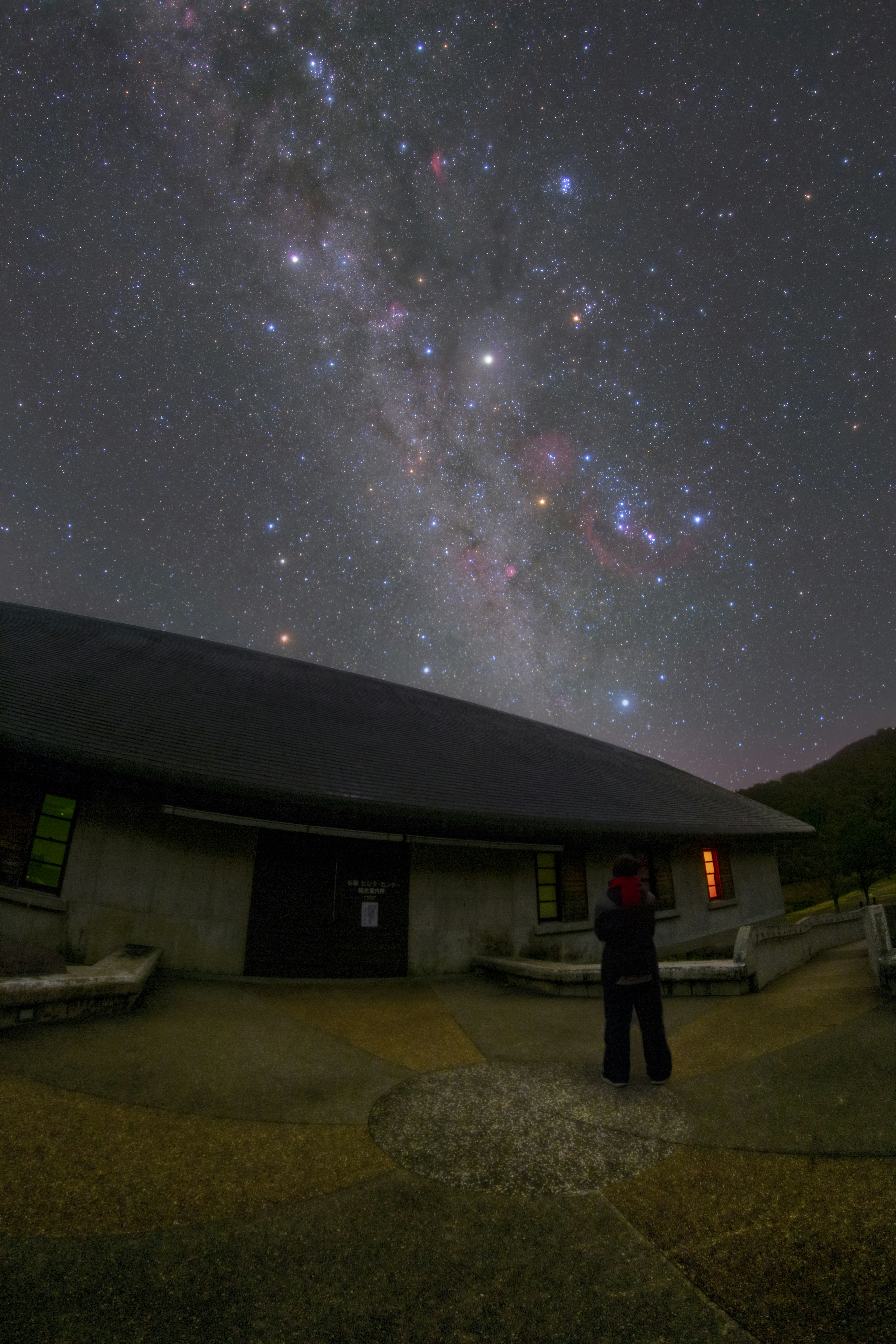 天の川が広がる夜空と屋外の建物前の人物
