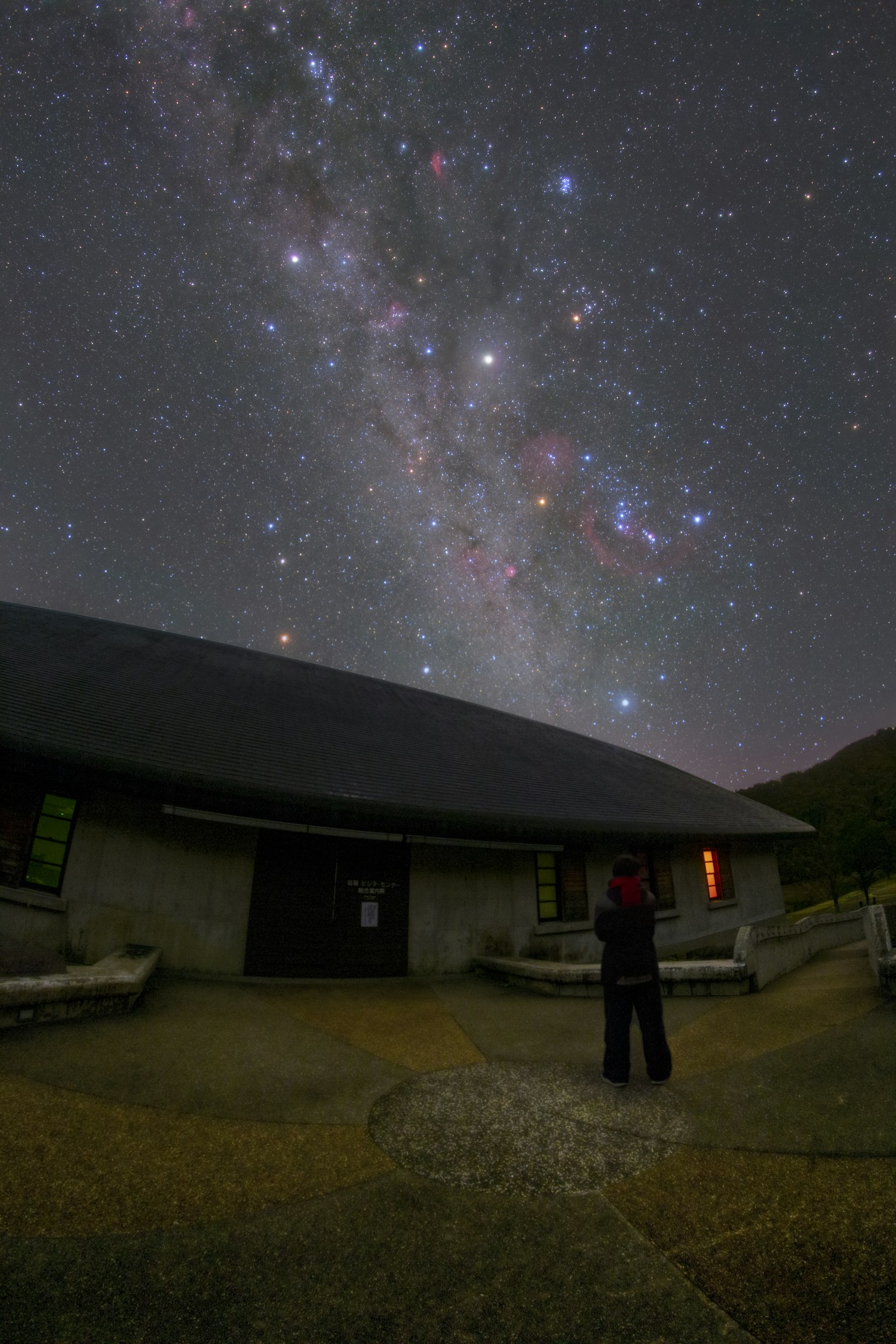 Personne regardant la Voie lactée sous un ciel étoilé avec un bâtiment au premier plan