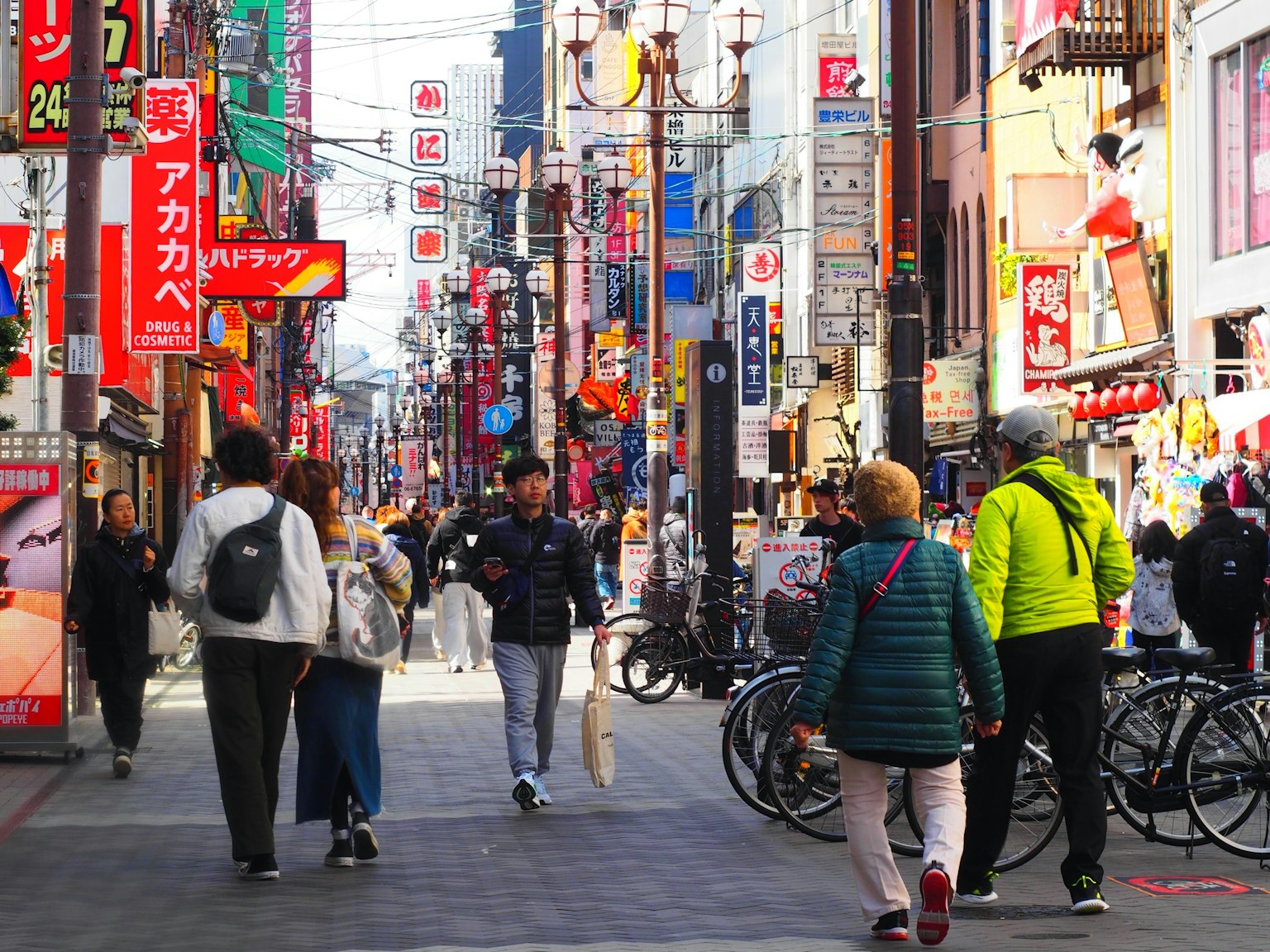 ฉากถนนที่คึกคักมีผู้คนเดินไปมาและป้ายสีสันสดใส