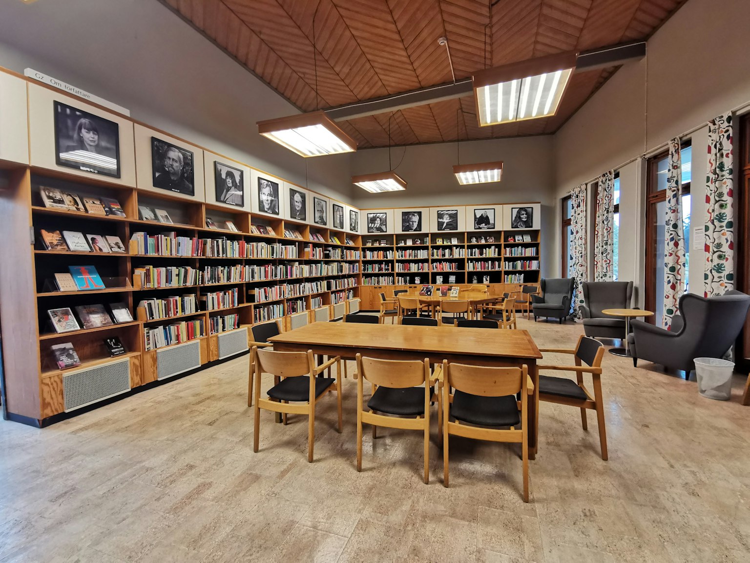 Interno di una biblioteca tranquilla con tavoli e sedie in legno scaffali di libri e fotografie incorniciate sulle pareti