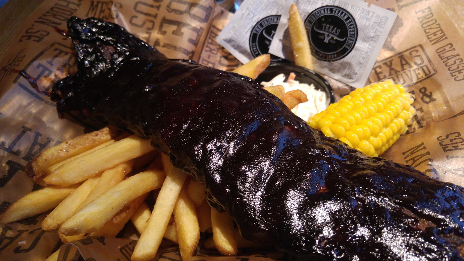 Schwarze BBQ-Rippchen serviert mit Pommes frites und Maiskolben