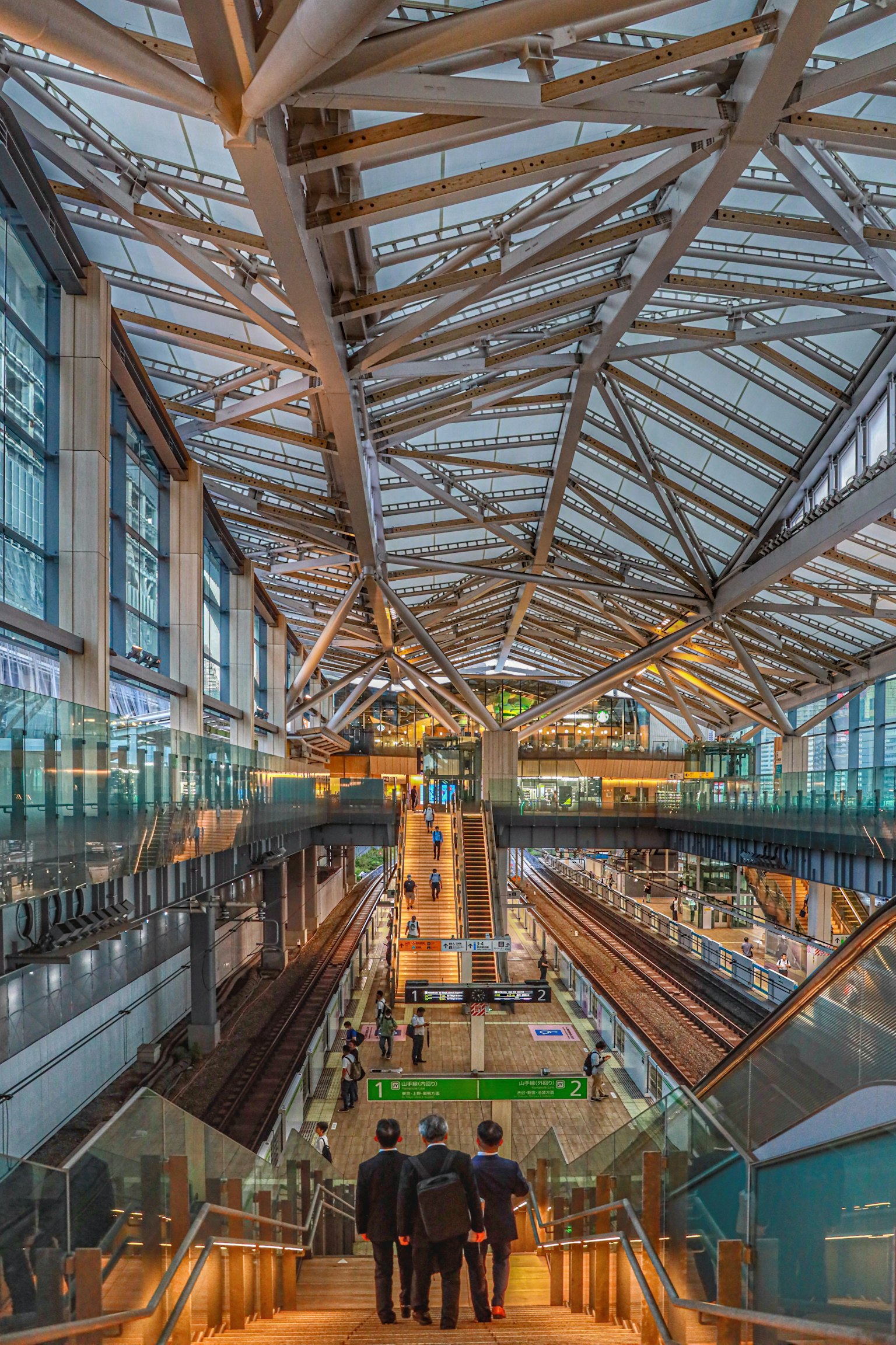 Vista interior de una estación de tren moderna con trusses metálicos y escaleras mecánicas