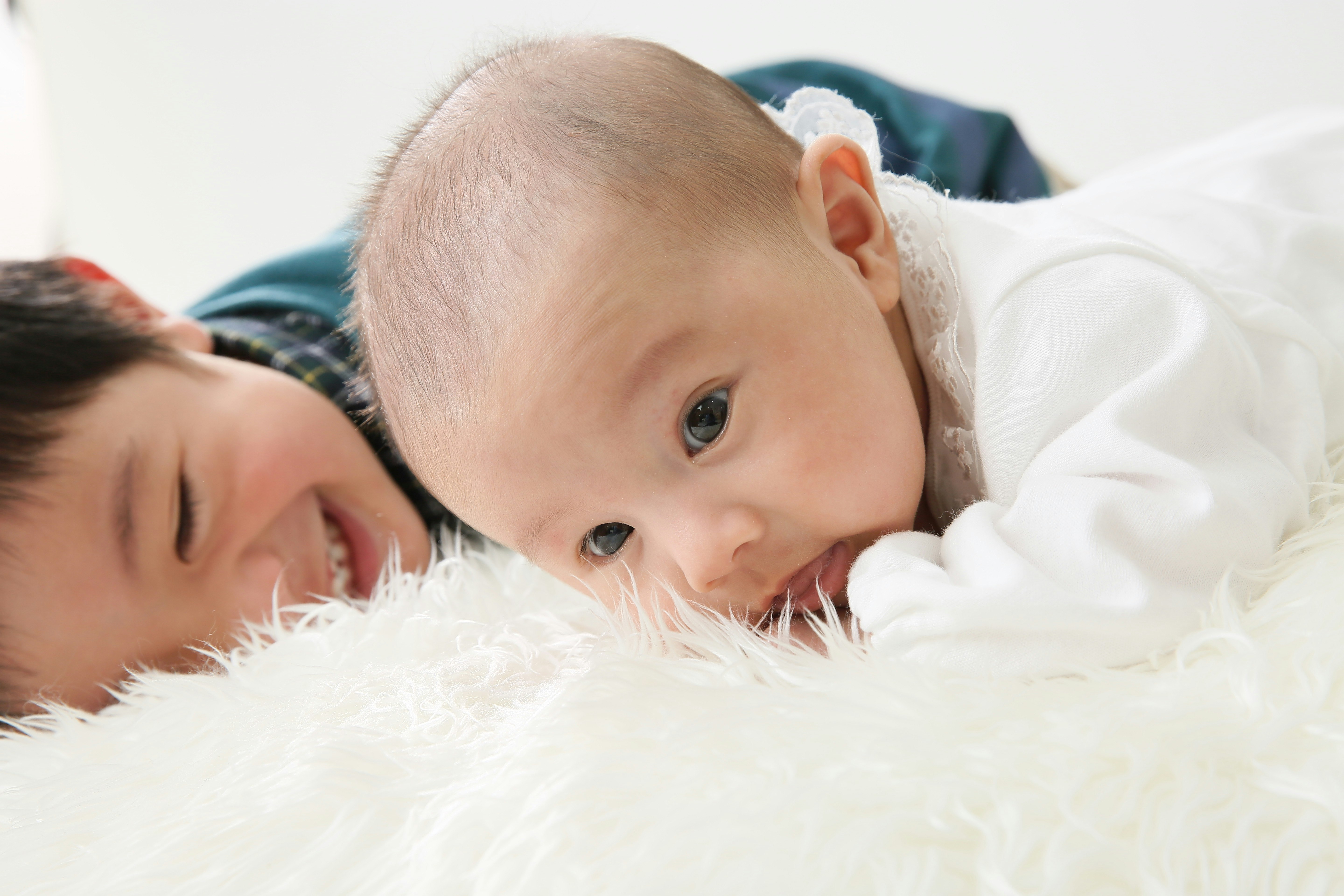 ふわふわの毛布の上で微笑む生後1ヶ月の赤ちゃんと兄妹の家族