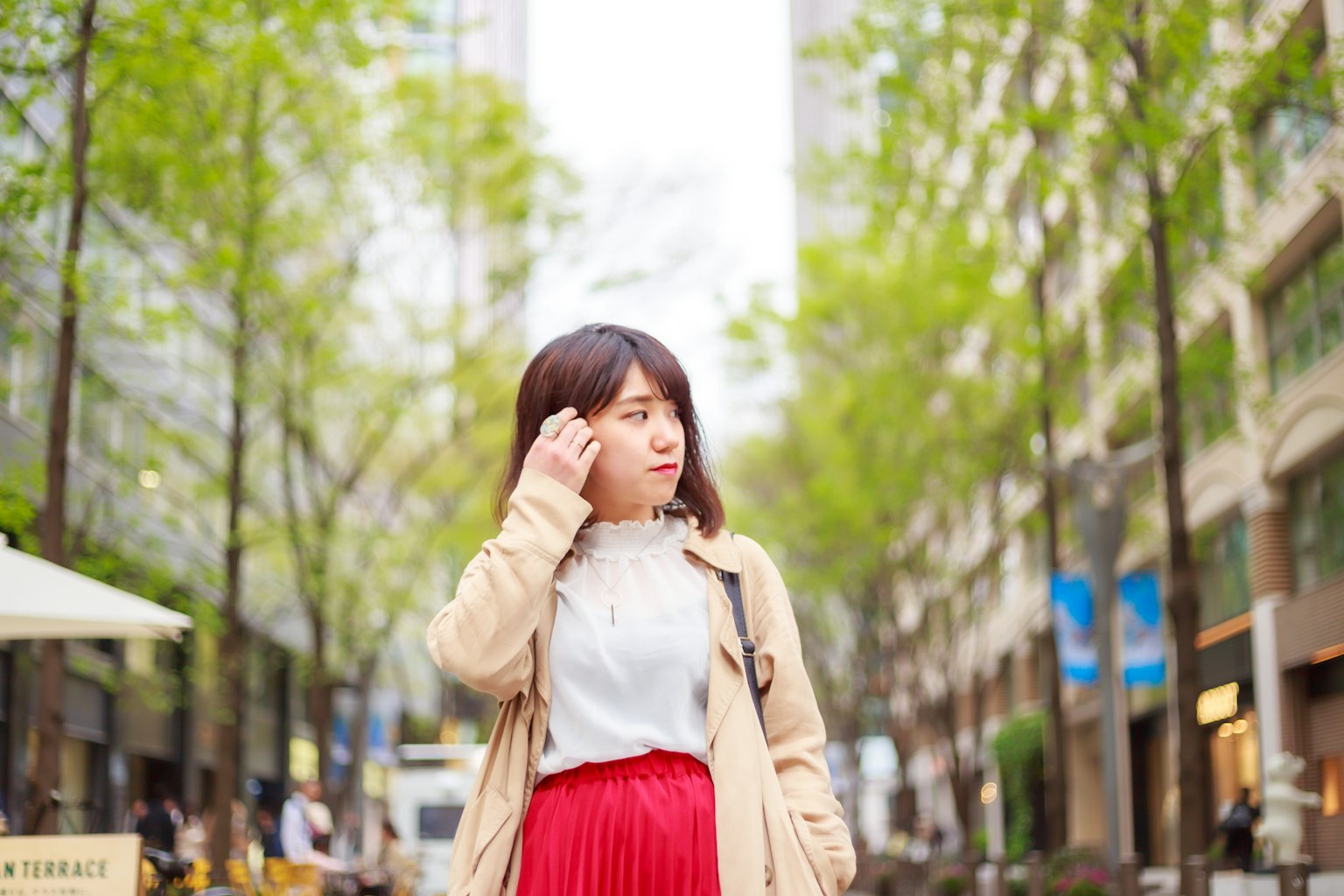 一位穿着红色裙子的女性站在被绿色树木环绕的街道上