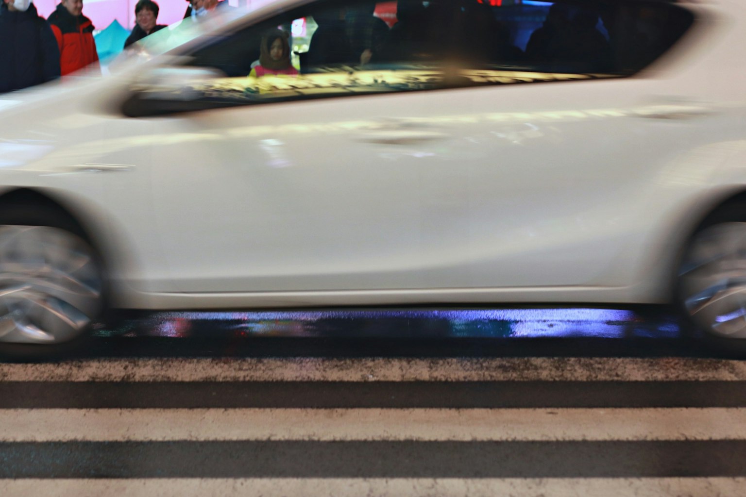 Un'auto bianca che attraversa un attraversamento pedonale in un ambiente urbano notturno