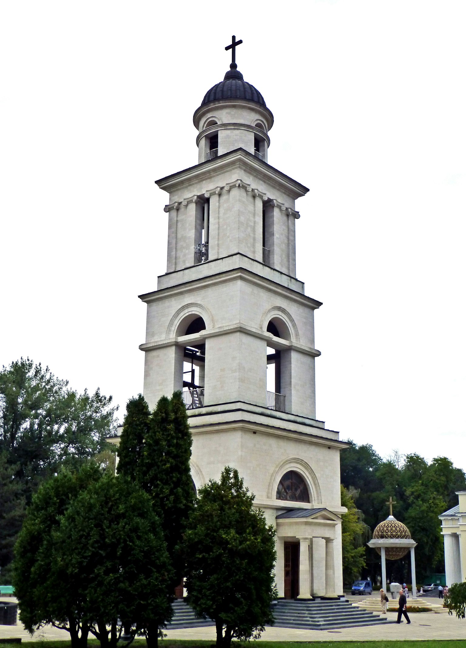 White stone bell tower with green trees in the foreground