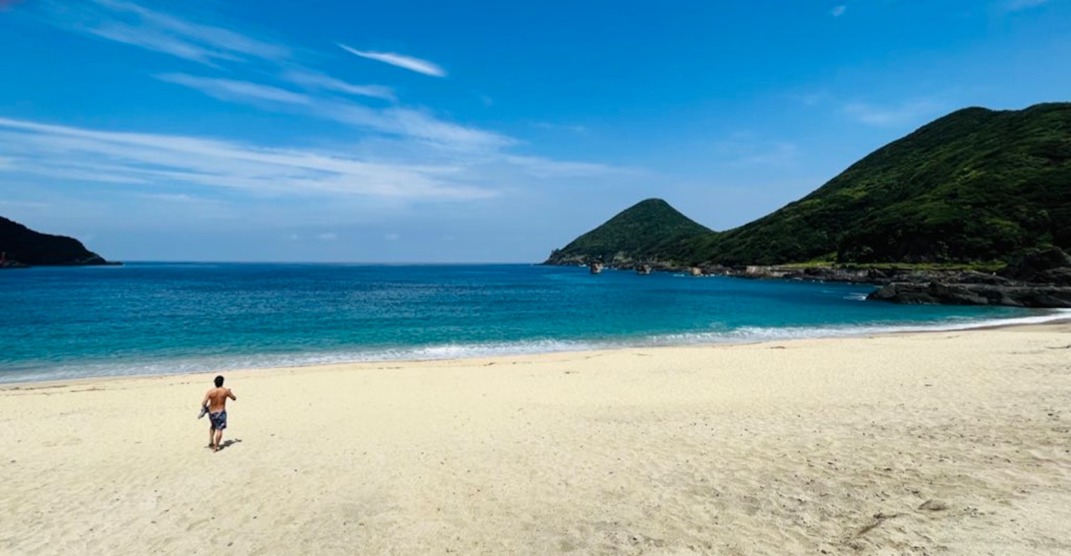Homme marchant sur une plage de sable avec un océan bleu et des montagnes en arrière-plan