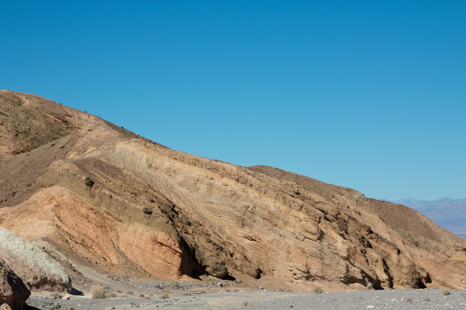 Paesaggio montano con strati di roccia colorati sotto un cielo blu chiaro