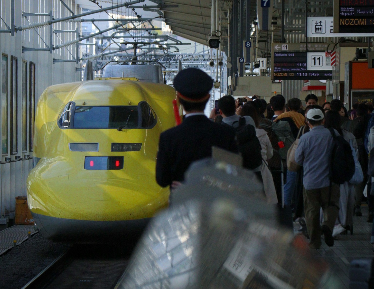 Scene of a yellow Shinkansen train at a station with passengers waiting