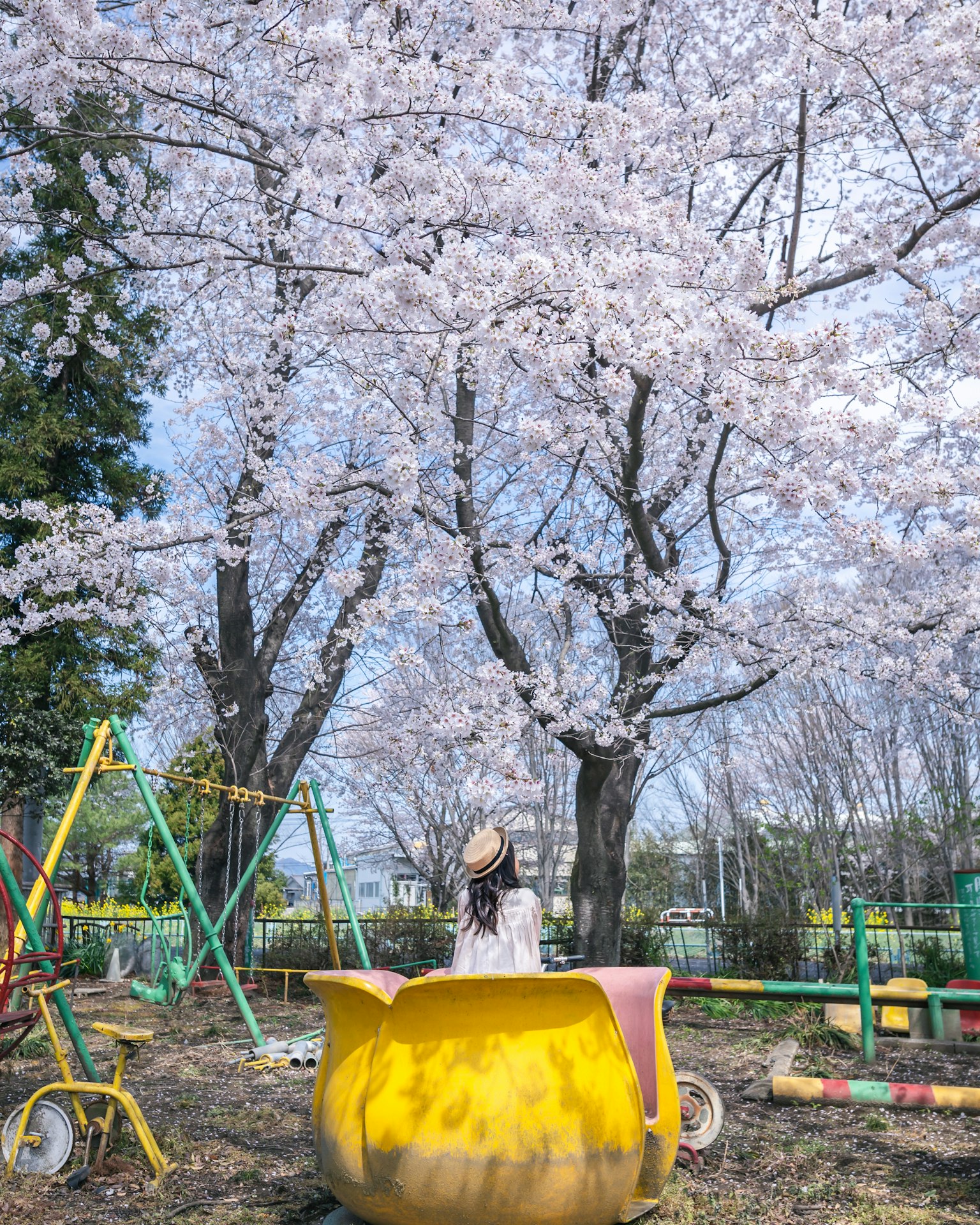 Kind spielt in einem Park mit Kirschblütenbäumen und Spielgeräten