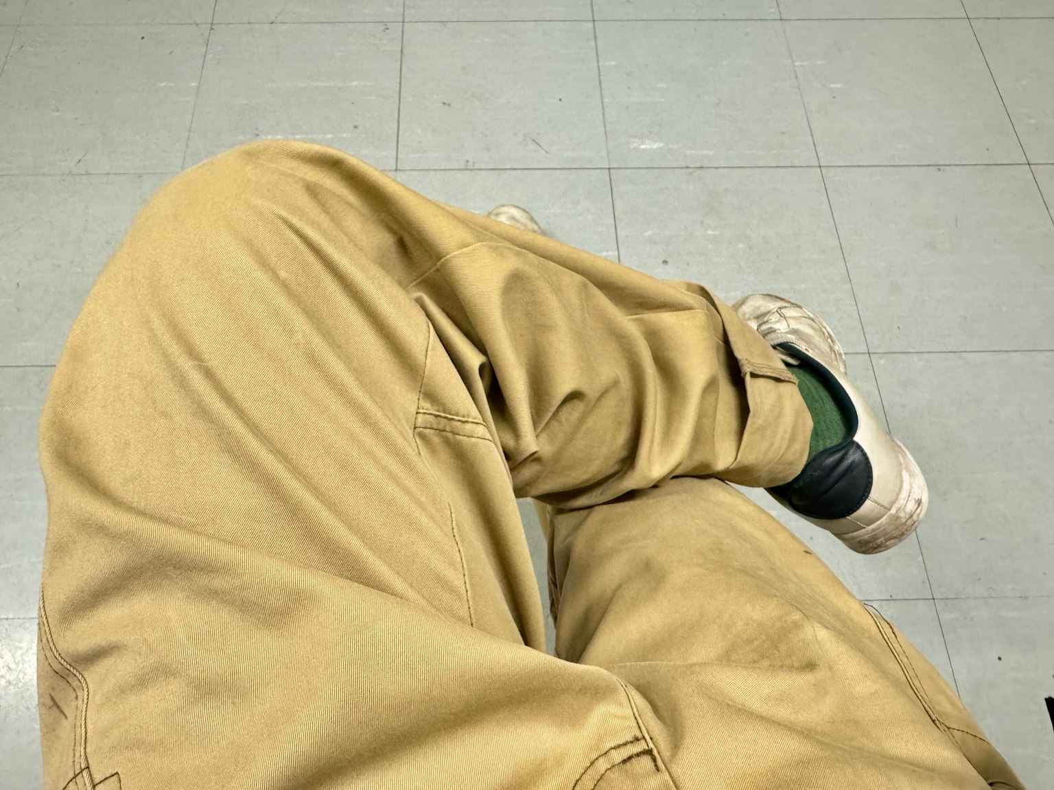 Vista ravvicinata delle gambe di una persona seduta su una sedia con pantaloni beige e scarpe bianche