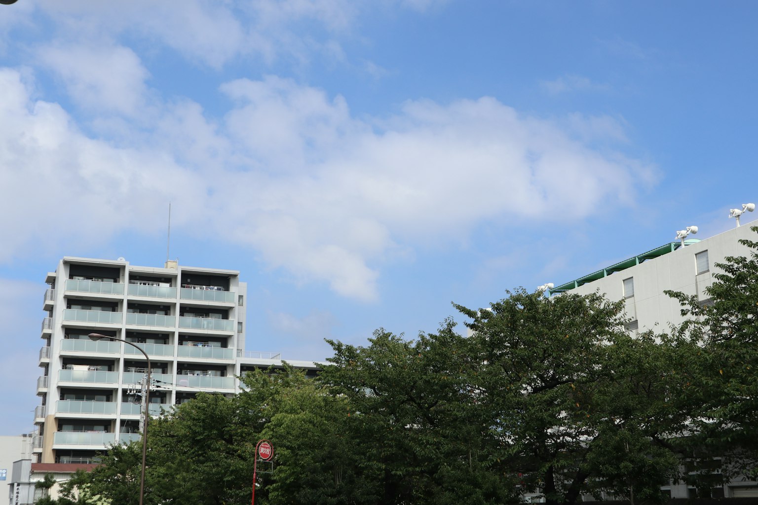 อาคารใต้ท้องฟ้าสีฟ้าพร้อมเมฆขาวและต้นไม้สีเขียว