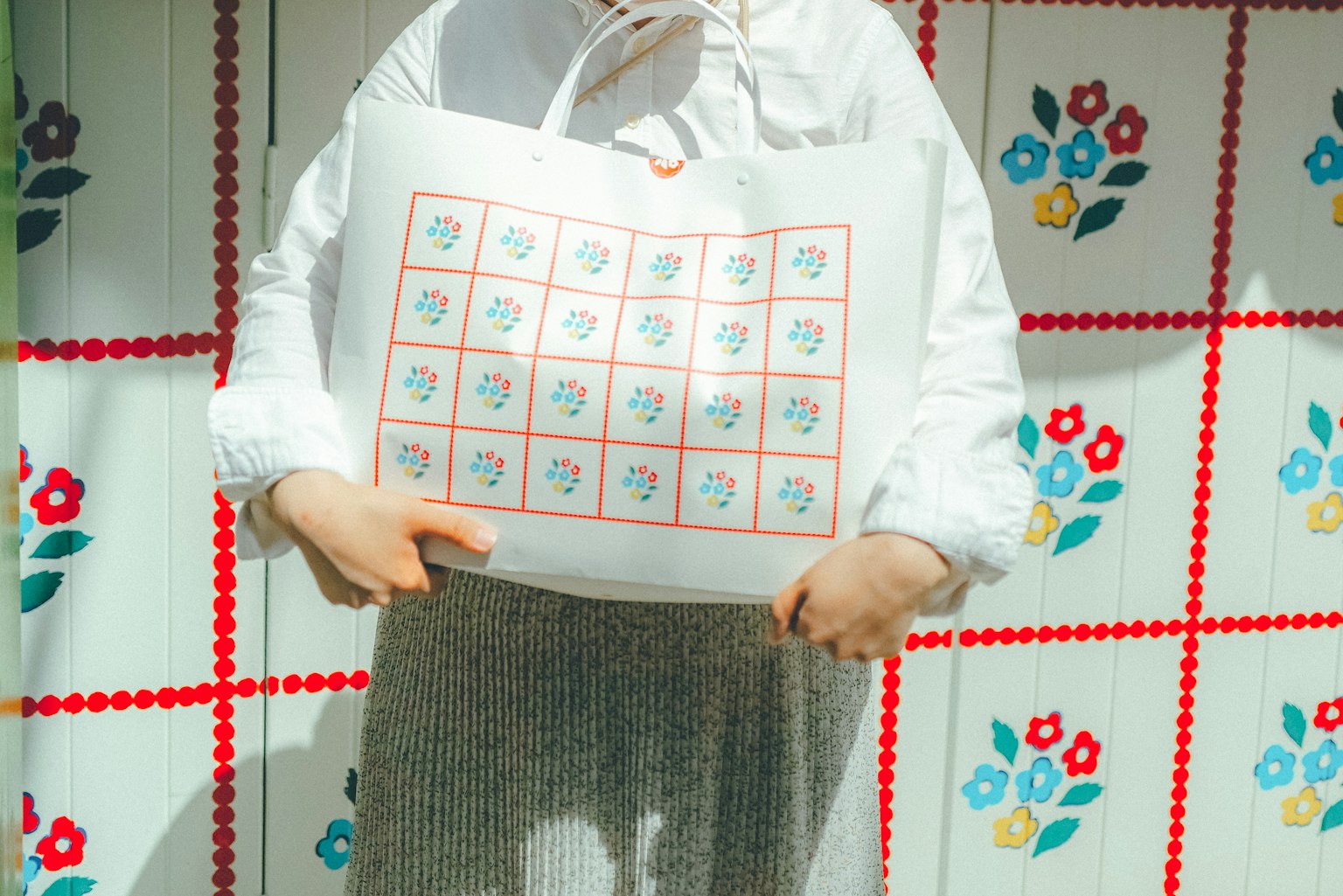 여성이 꽃무늬가 있는 배경에서 다채로운 디자인의 토트백을 들고 있다