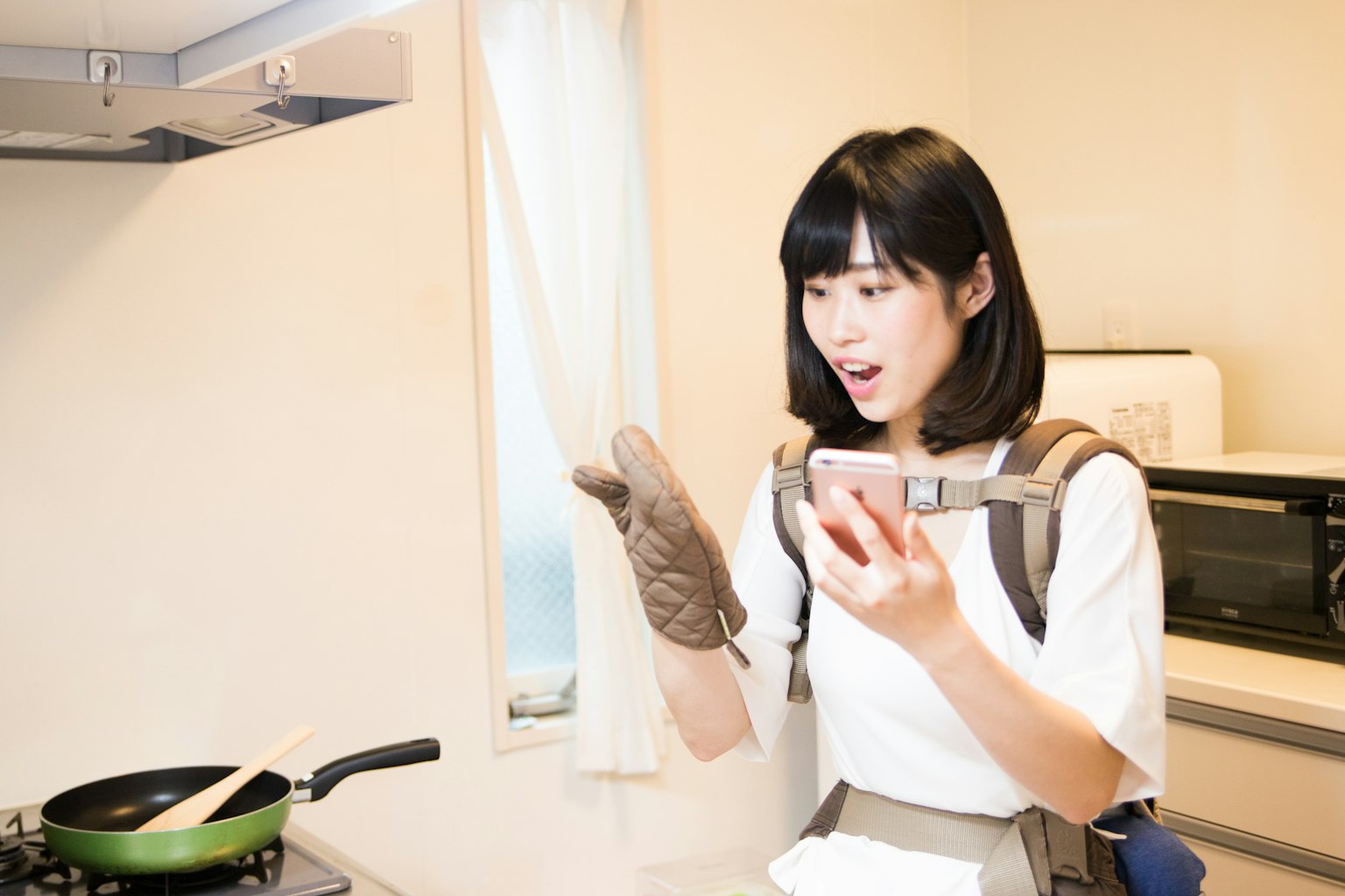 Mujer cocinando en la cocina mirando sorprendida su smartphone