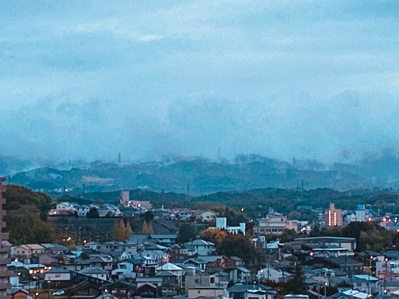 A view of a residential area with houses under a blue sky and cloudy mountains in the background