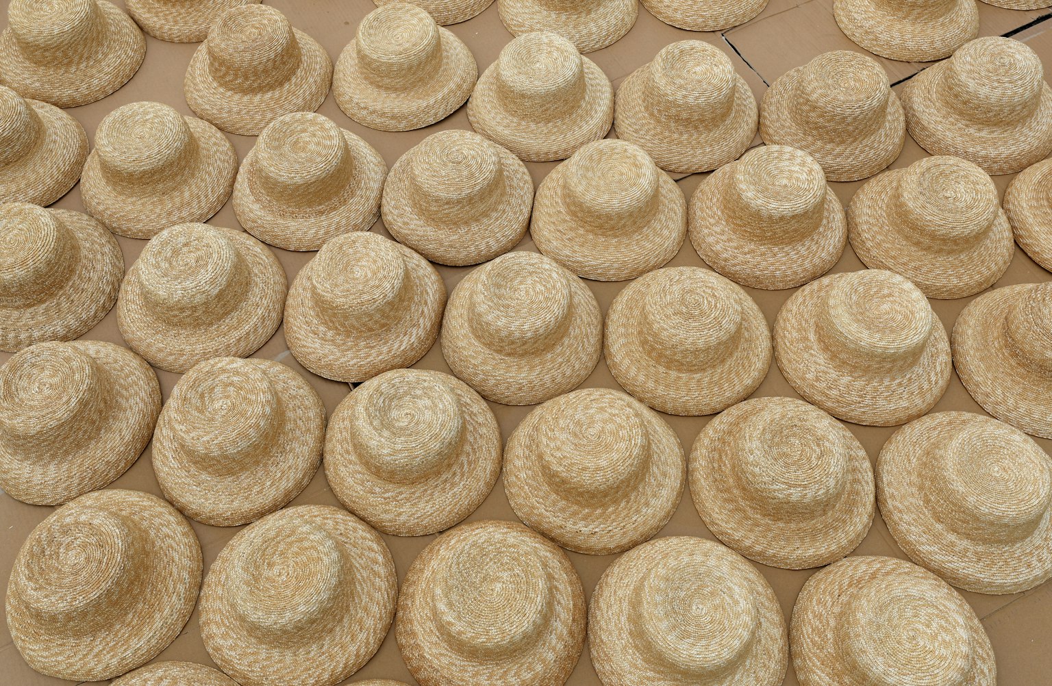A large number of straw hats arranged neatly on a surface