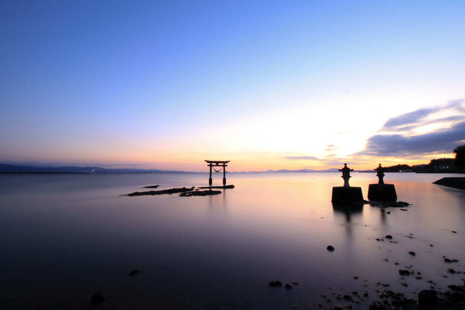 Paysage serein au crépuscule avec un torii et des silhouettes de lanternes en pierre au bord de la mer tranquille