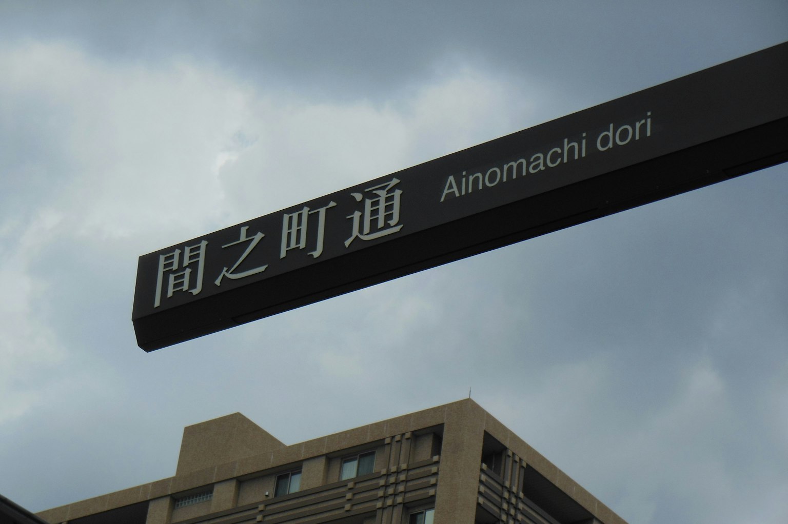 Señal de calle para Ainomachi dori con cielo nublado