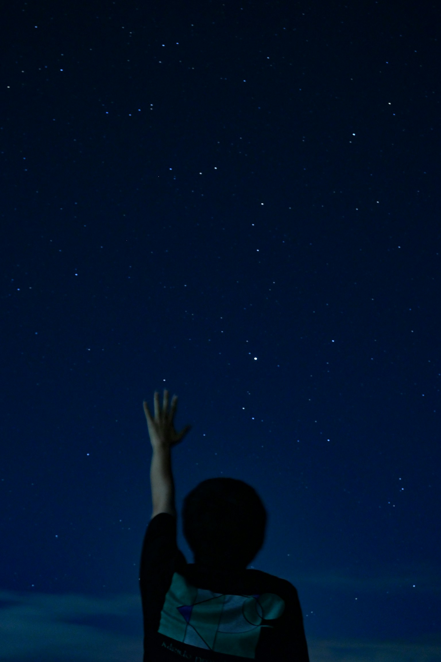 一个男孩在夜空中伸手去摘星星的轮廓