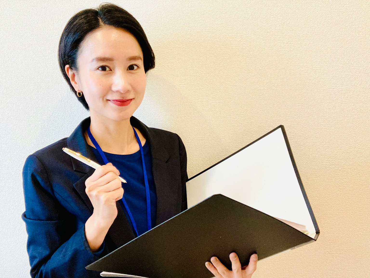 A business-attired woman smiling while holding a notebook and pen