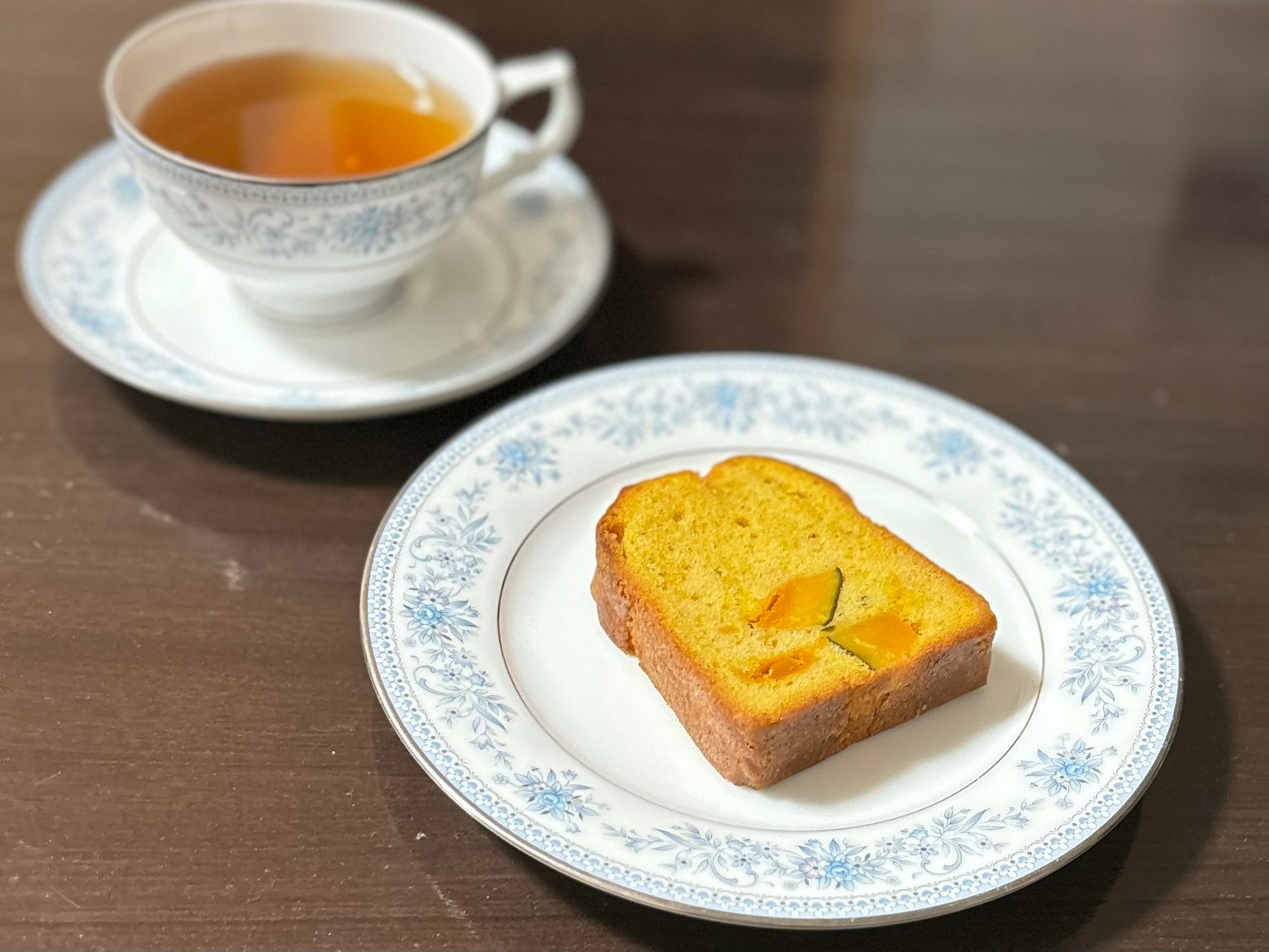一杯茶和一片橙色蛋糕放在装饰盘上的图片