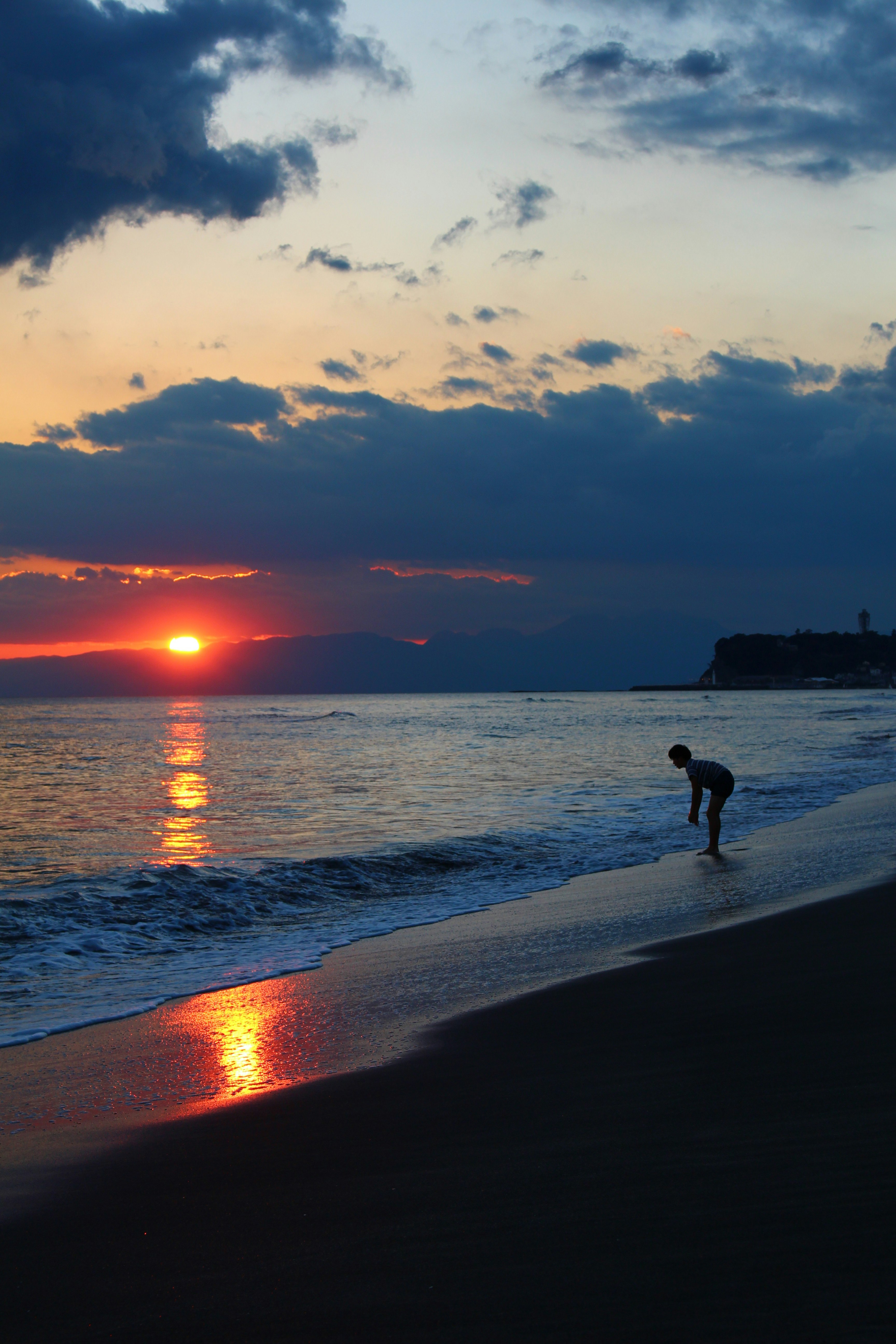 夕暮れの海辺で一人で歩く人と水平線の夕日