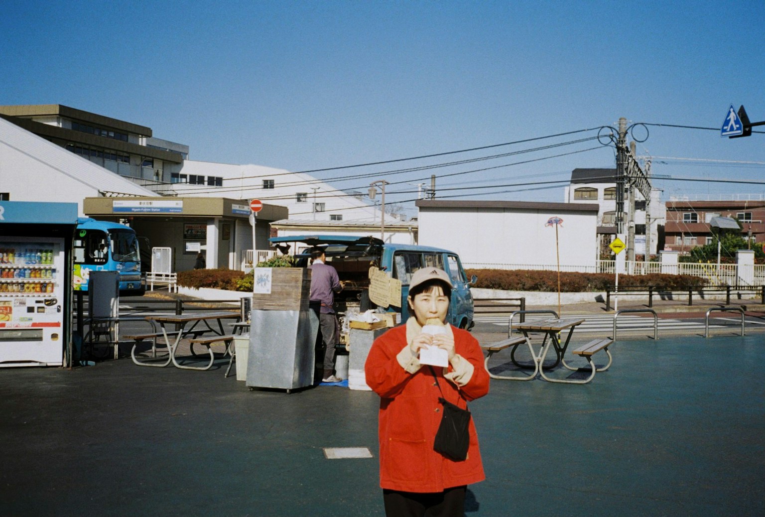 青空の下で食べ物を持つ赤い服の女性と屋台の風景