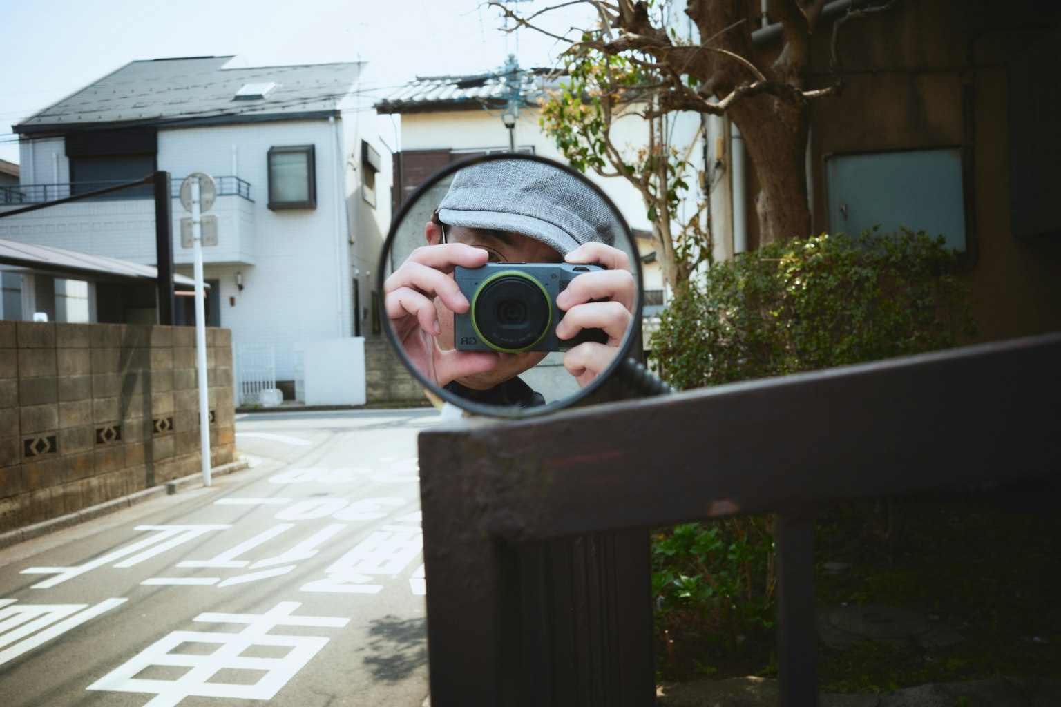 Reflection of a person holding a camera in a mirror with surrounding houses