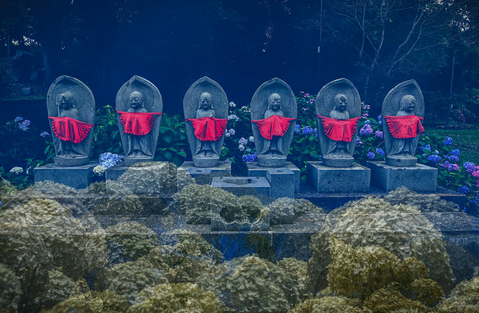 Sechs Steinstatuen mit rotem Tuch in einem Garten