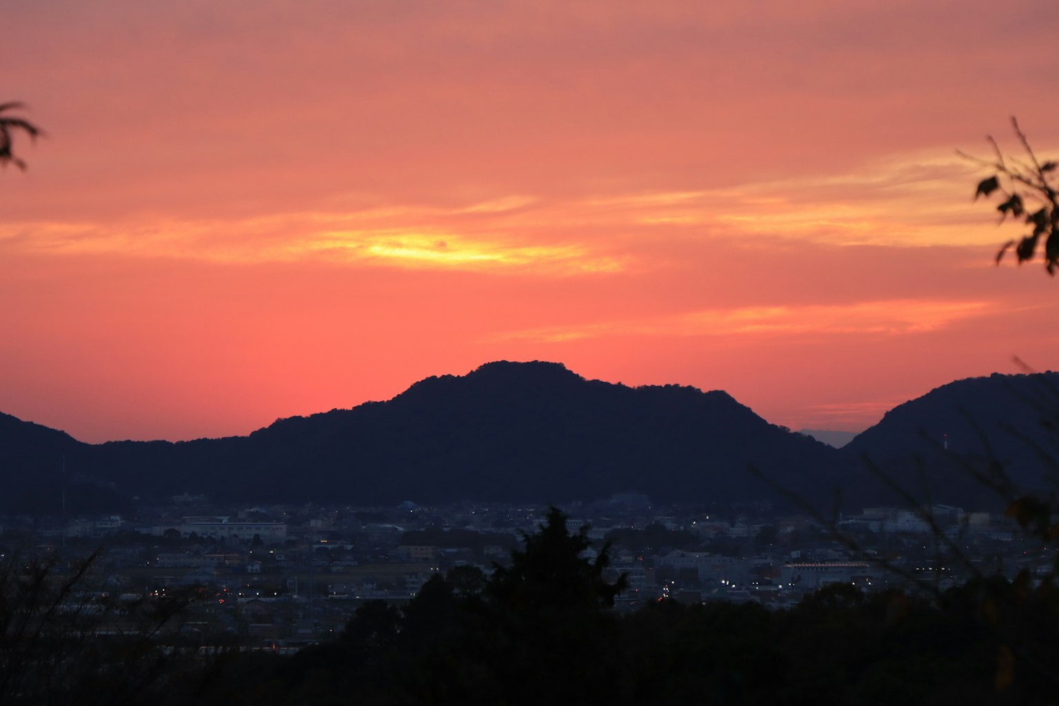 夕焼けに染まる山々のシルエットと街の光