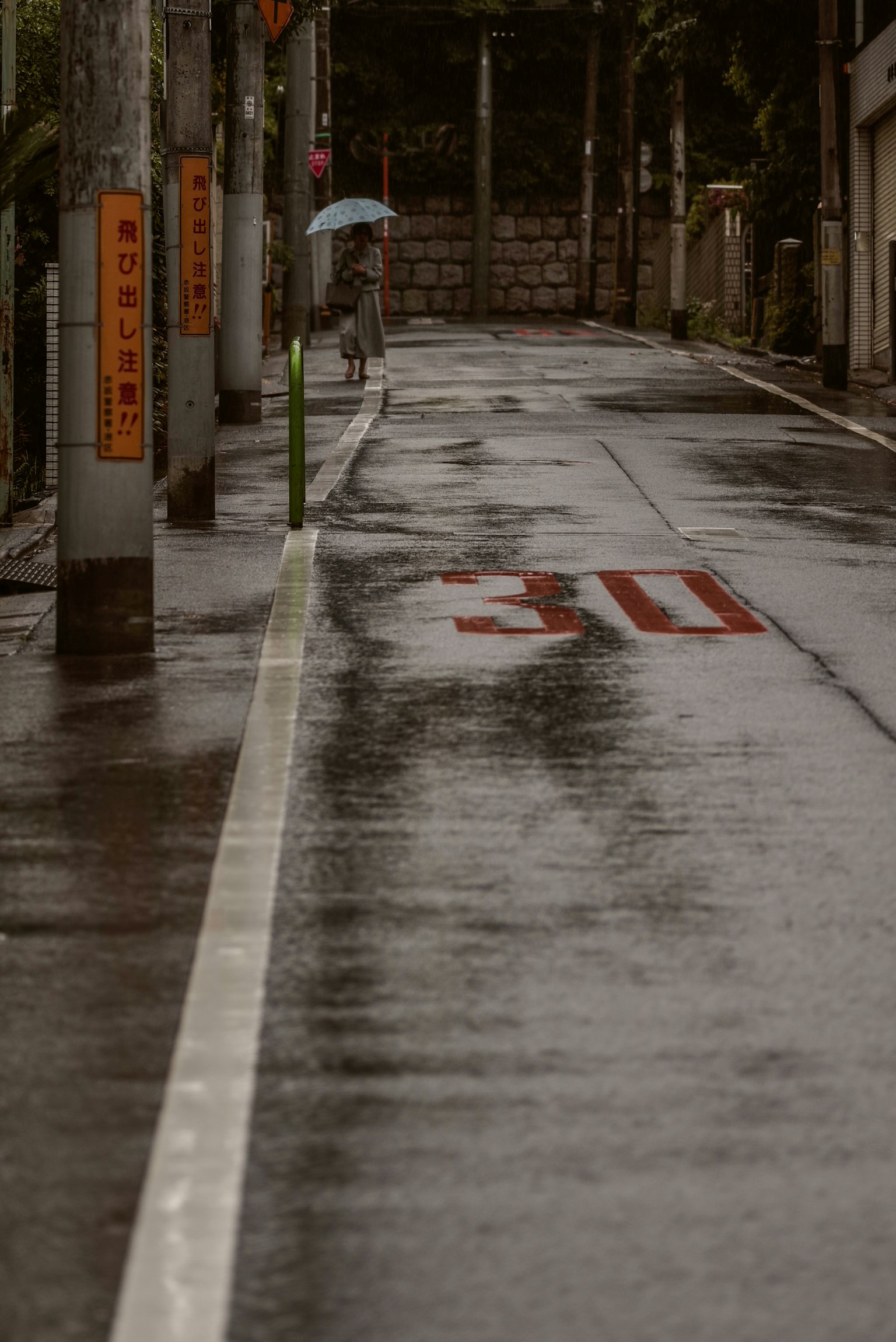 A quiet road wet from rain with a person holding an umbrella