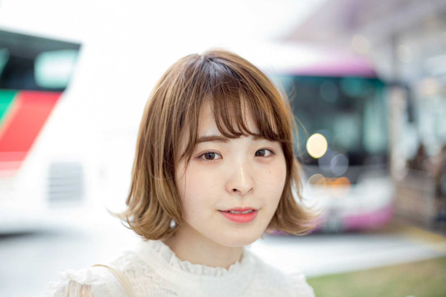 Nahaufnahme einer lächelnden Frau in einem Park mit kurzem Haarschnitt heller Hintergrund mit Bussen