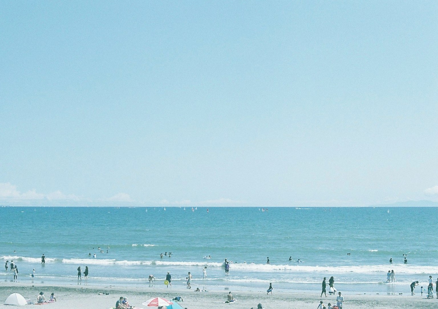 Beach scene with people enjoying the blue ocean and sky