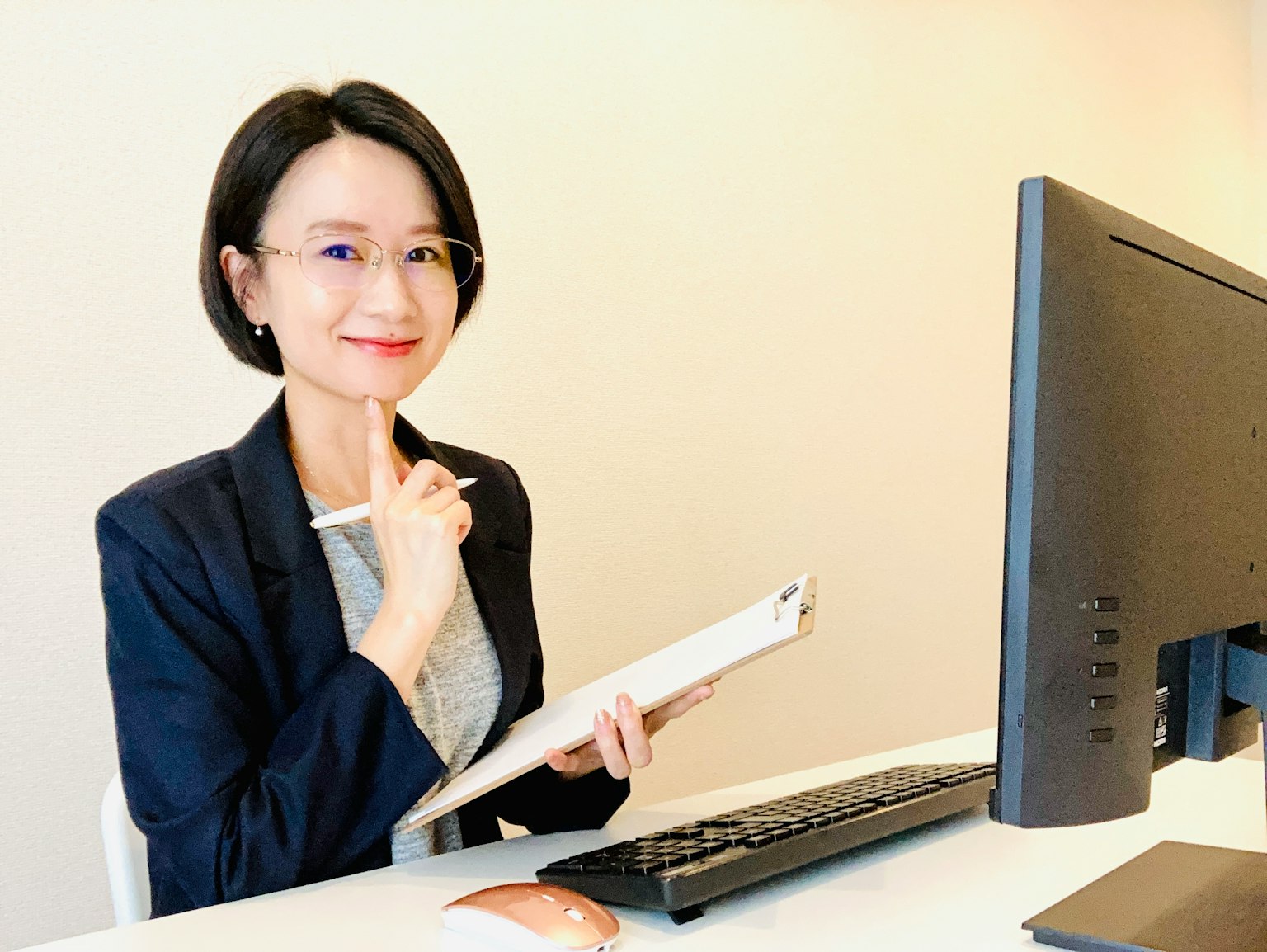 Donna sorridente davanti a una scrivania con un computer che tiene un taccuino