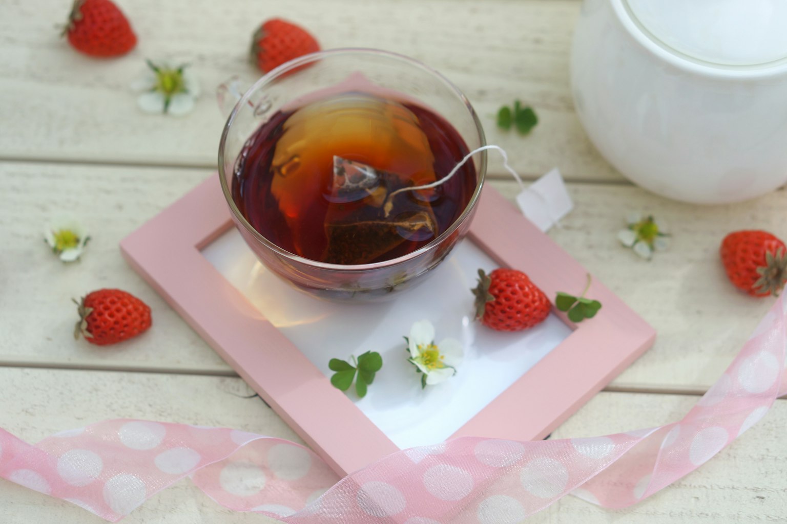 Transparente Tasse mit Teebeutel und Erdbeeren auf einem Tisch angeordnet