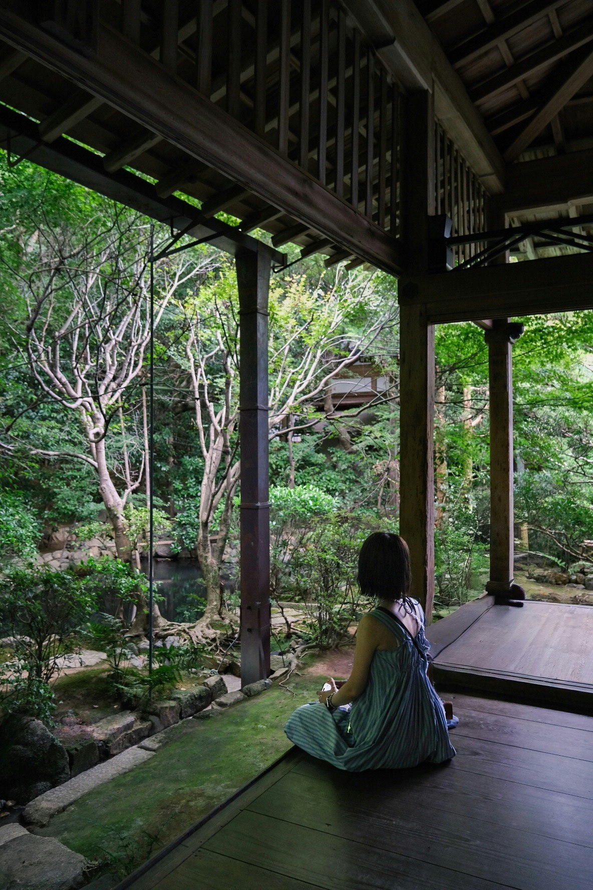 穿和服的女性坐在走廊上，凝望有樹木的庭院