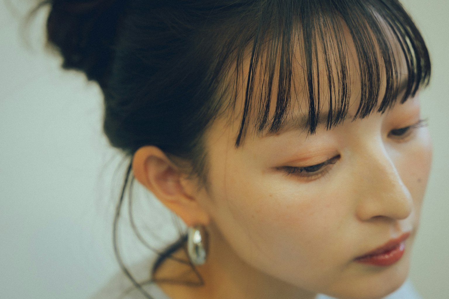 Close-up wanita dengan poni, riasan halus, anting perak, ekspresi lembut