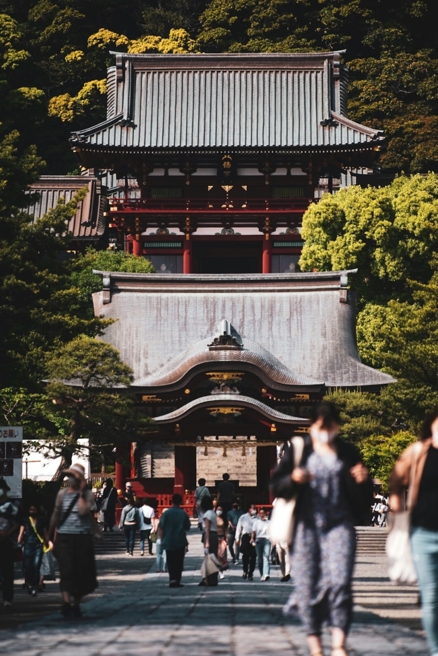 Traditional Japanese shrine entrance surrounded by greenery with visitors